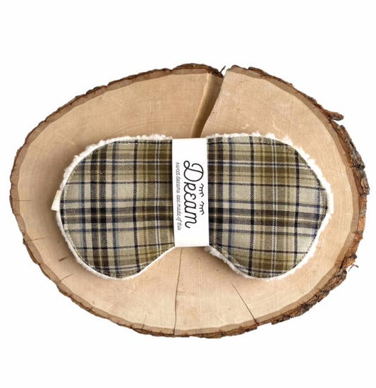 Plaid Cotton Sleep Mask for Relaxation featuring a green and beige tartan pattern, wrapped with branded label on a wood slice.