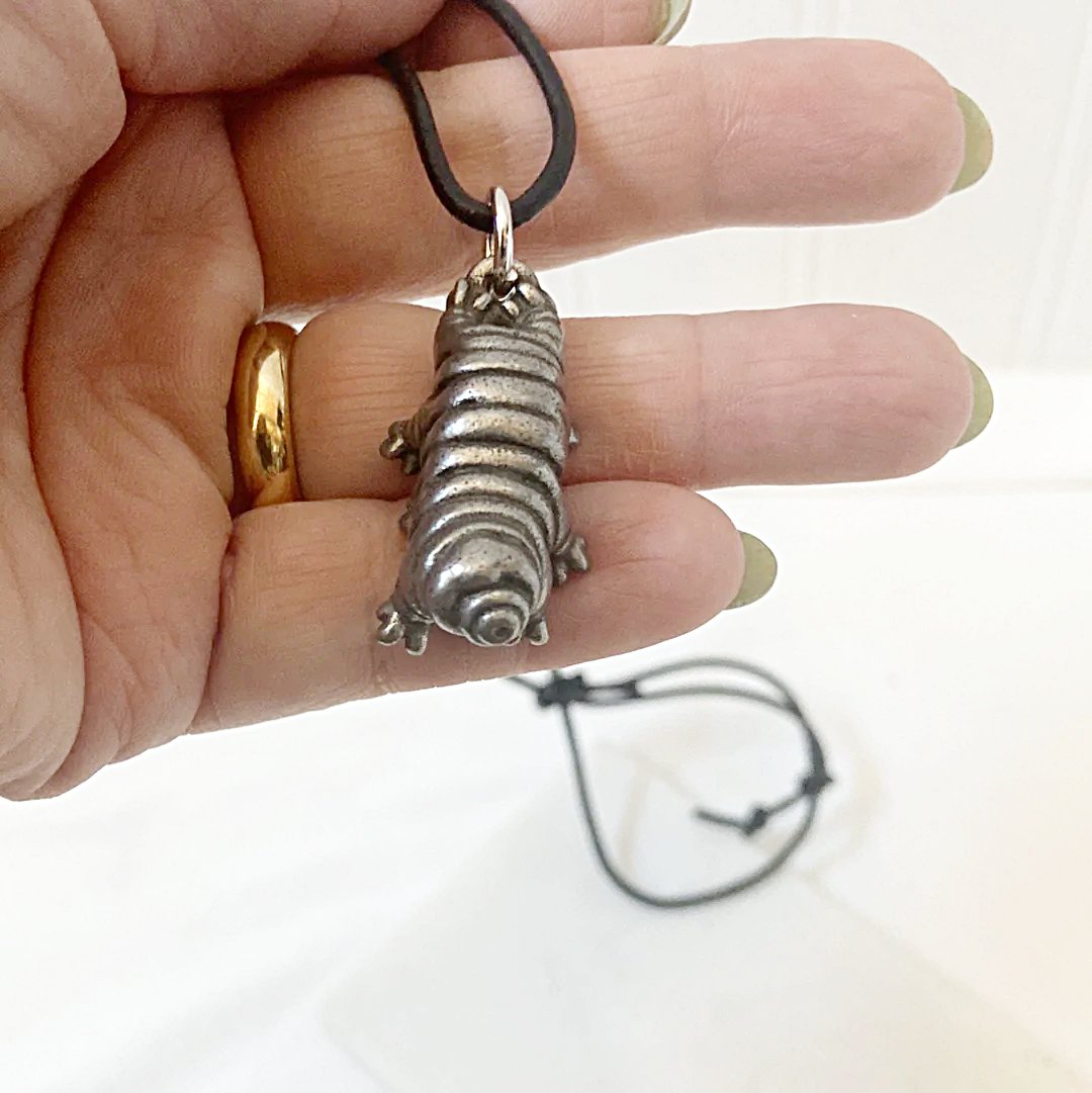 Hand holding Tardigrade Necklace to show size and detail. Features a metallic water bear charm symbolizing strength and survival.