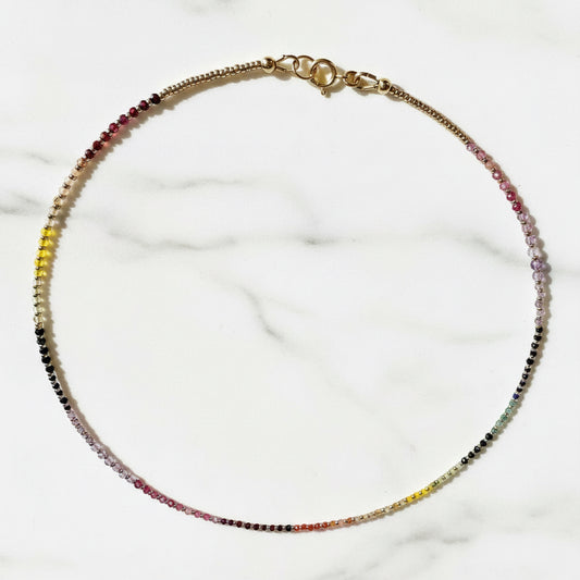 Close-up of gemstone rainbow necklace with gold clasp on white background