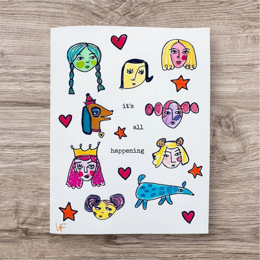 Inspirational Good Vibe Tribe Card featuring whimsical hand-painted faces, stars, hearts, and text 'it's all happening' for uplifting messages.