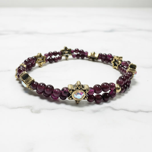 Close-up of garnet gemstone stretch bracelet with gold star and iridescent bead details