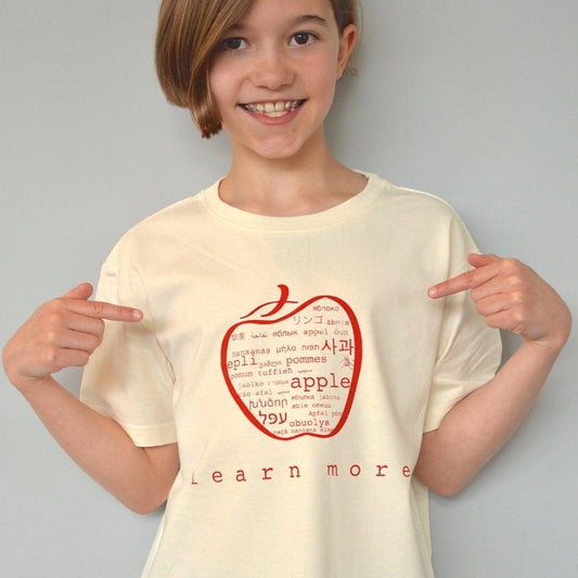 Child wearing cream Kids' Apple Organic Cotton T-Shirt with red apple graphic and 'learn more' text. Sustainable educational top by Uni-T.