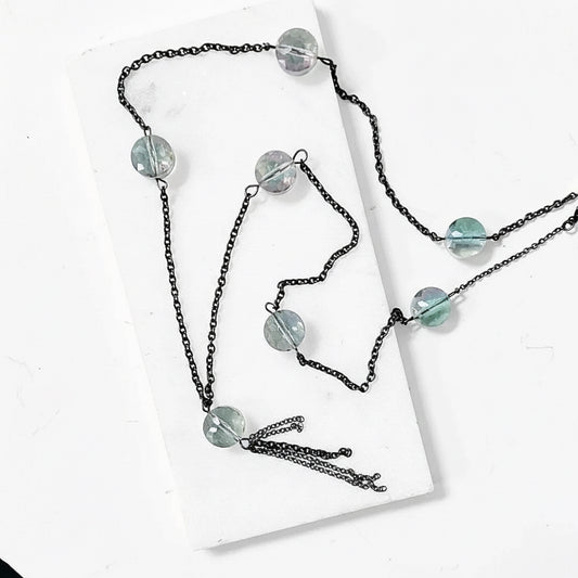 Long crystal chain necklace with pink, green, and yellow beads on a darkened brass chain, displayed on a white background for layering jewelry.