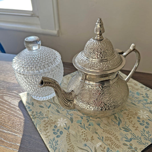 Silver teapot with engraved floral pattern on cloth