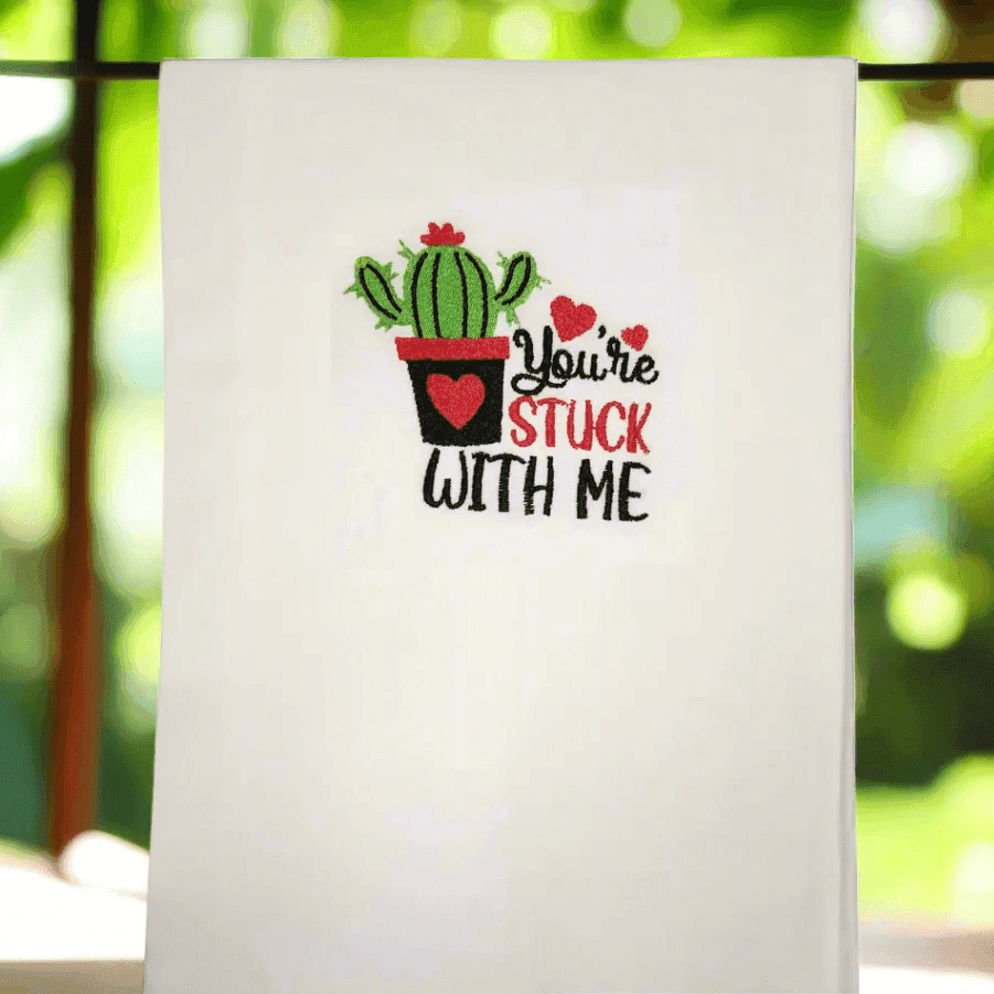 You're Stuck With Me embroidered towel featuring cute cactus and heart design, hanging with natural light. Fun kitchen decor or gift idea.