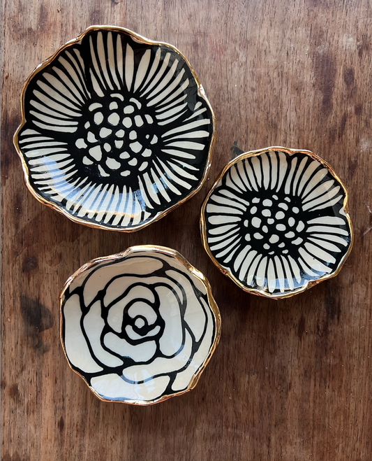Three 3" handmade flower-shaped jewelry dishes with bold black floral designs and 22K gold rims, perfect for organizing small accessories.