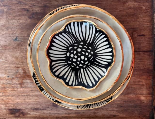 Top view of stacked 4" handmade ceramic dishes with bold black floral designs and 22K gold trim, perfect for gifting or decor.