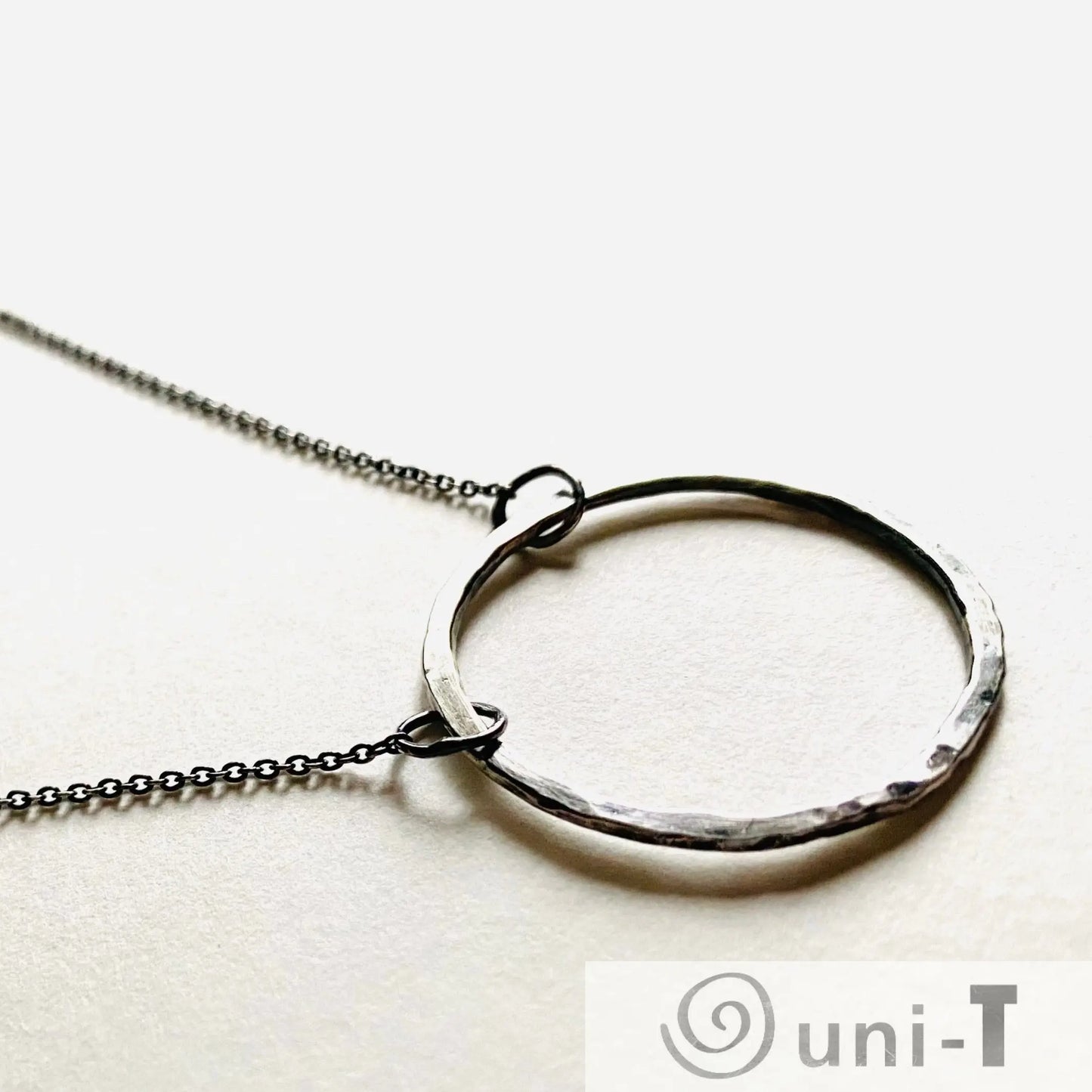 Close-up of large hammered sterling silver circle pendant on fine chain, minimalist infinity necklace design by Uni-T.