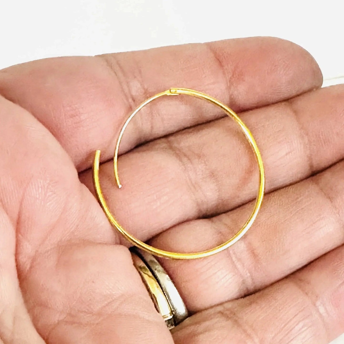Close-up of lightweight gold filled hoop earring with hinge clasp, shown in hand to highlight size and golden finish.