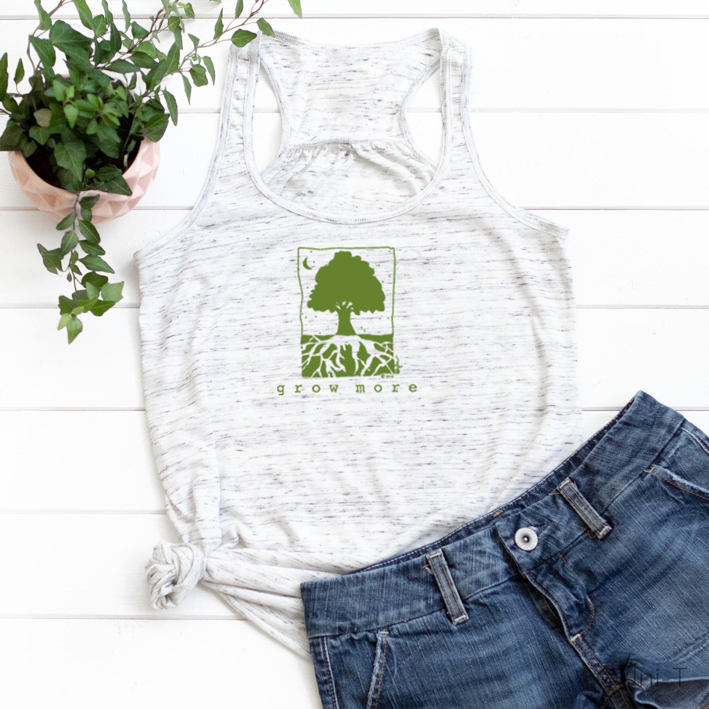 White speckled "Grow More" flowy tank top styled with denim shorts, featuring green tree graphic for gardening and growth enthusiasts.