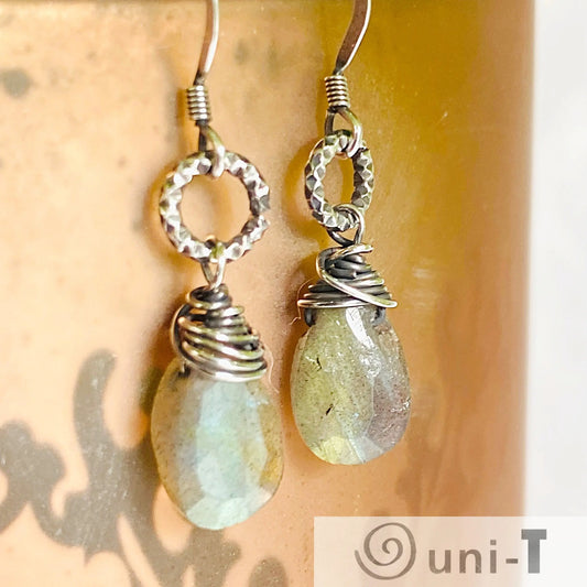 Close-up of wire wrapped labradorite earrings featuring hammered silver rings and shimmering green-blue gemstone drops for a rustic chic look.