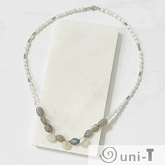 Labradorite and pearl necklace with adjustable length, displayed on a white stone slab to highlight gemstone details and silver clasp.