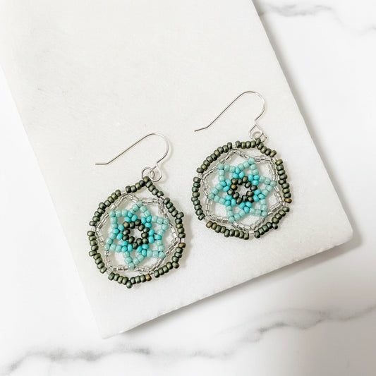 Seafoam green medallion earrings with sterling silver hooks and intricate blue and green floral beadwork, displayed on a white marble background.