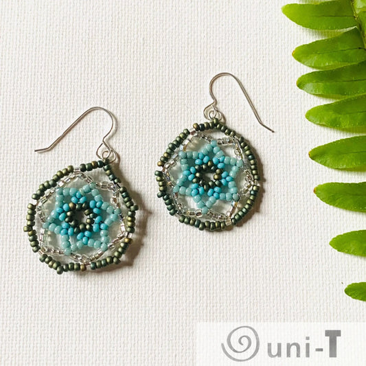 Sterling silver seafoam green medallion earrings featuring multicolor floral beads in green and blue, styled with a fern leaf for a natural look.