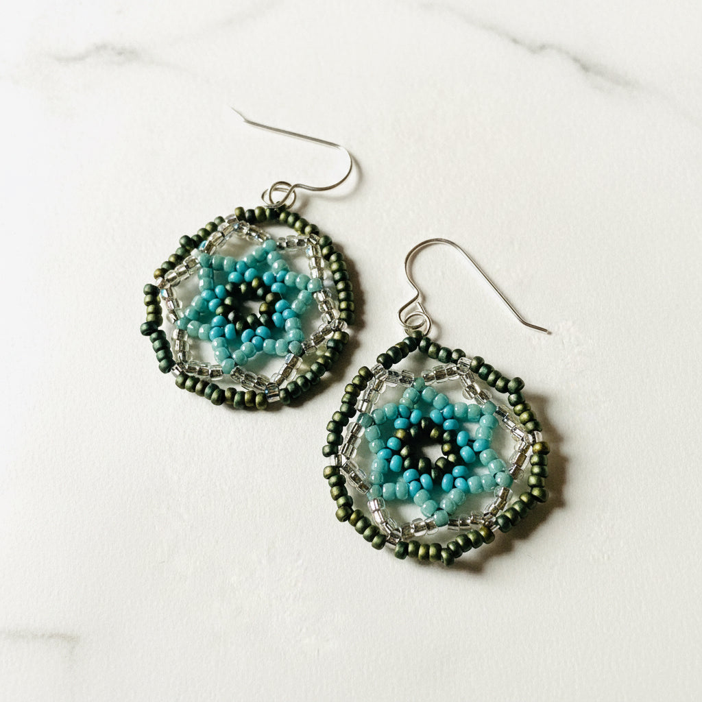 Close-up of seafoam green medallion earrings with detailed blue and green beaded flower design and silver ear wires, highlighting craftsmanship.