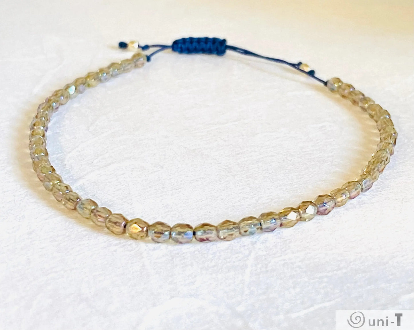 Stackable micro glass friendship bracelet with shimmering beads and adjustable navy thread, stylish and secure fit.