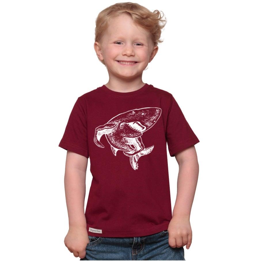 Smiling child wearing Kids' Shark Organic Cotton T-Shirt in maroon with white shark print. Eco-friendly animal lover tee by Uni-T.