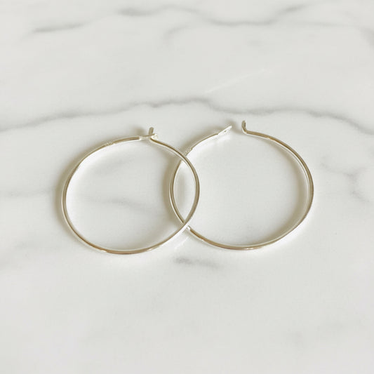 Pair of simple sterling silver hoops, 3/4” diameter, displayed flat on white background. Classic minimalist earrings in fine 22 gauge silver.