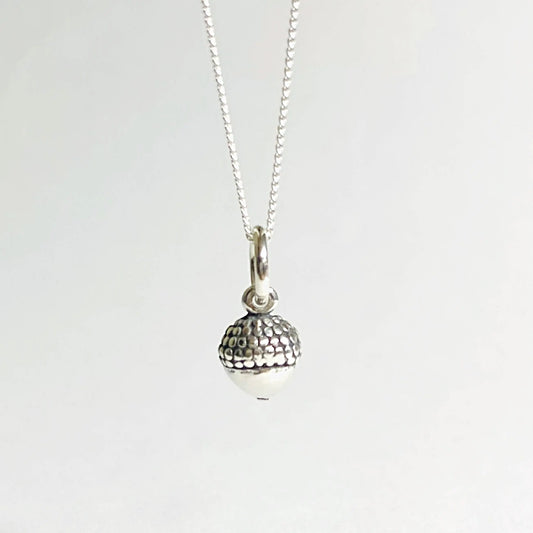 Close-up of sterling silver tiny acorn charm necklace, showcasing detailed texture and minimalist nature-inspired design.