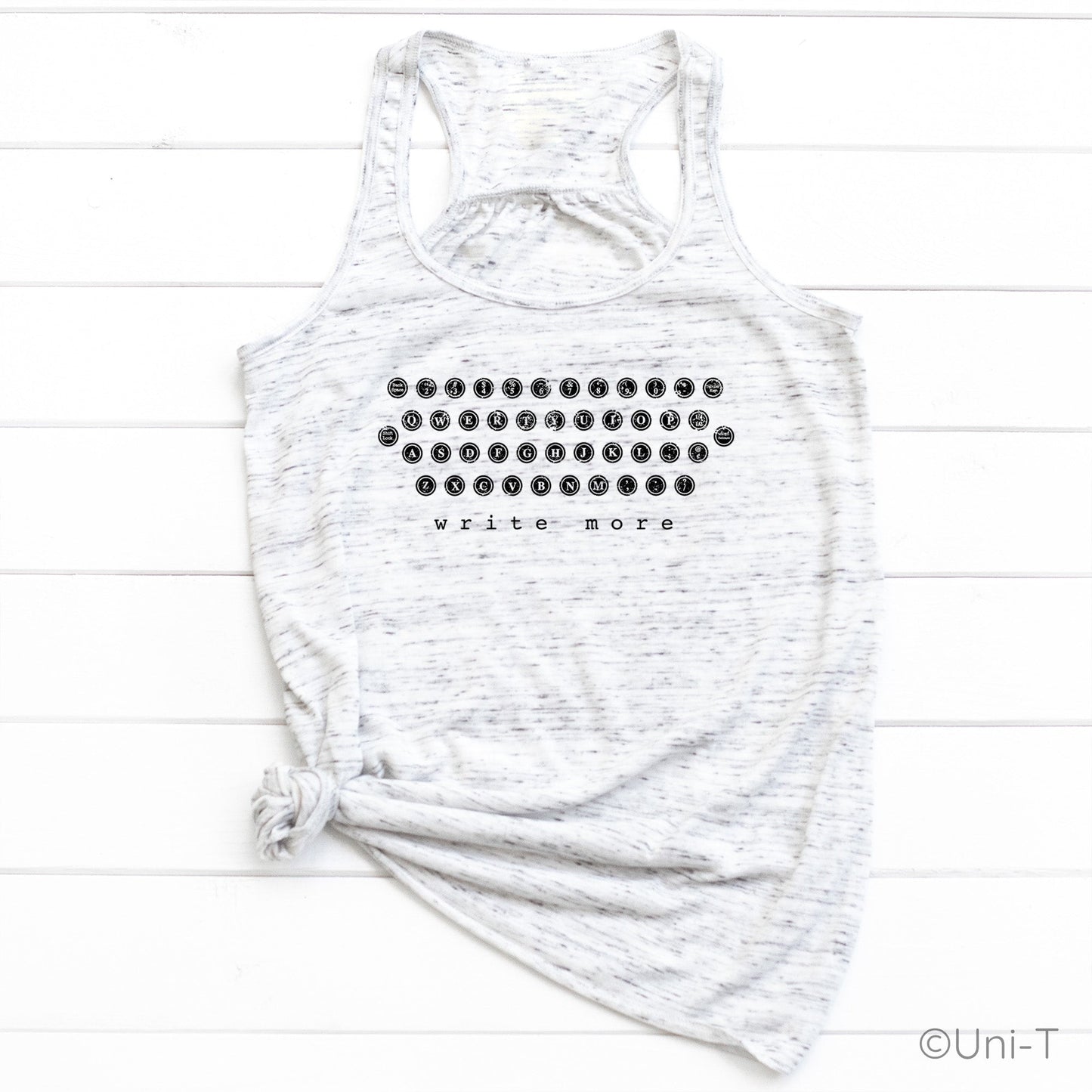 White speckled "Write More" tank top tied at the hem, showcasing a retro typewriter key graphic. Ideal for casual writer fashion.
