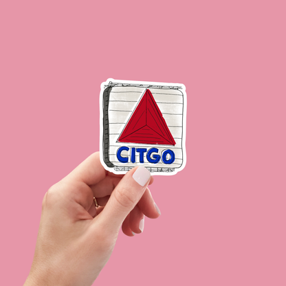 A hand with light nail polish holds the Copper & Print Sticker Fenway Citgo Sign Decor—a waterproof vinyl sticker of the iconic red-triangle CITGO sign on white—set against a solid pink background.