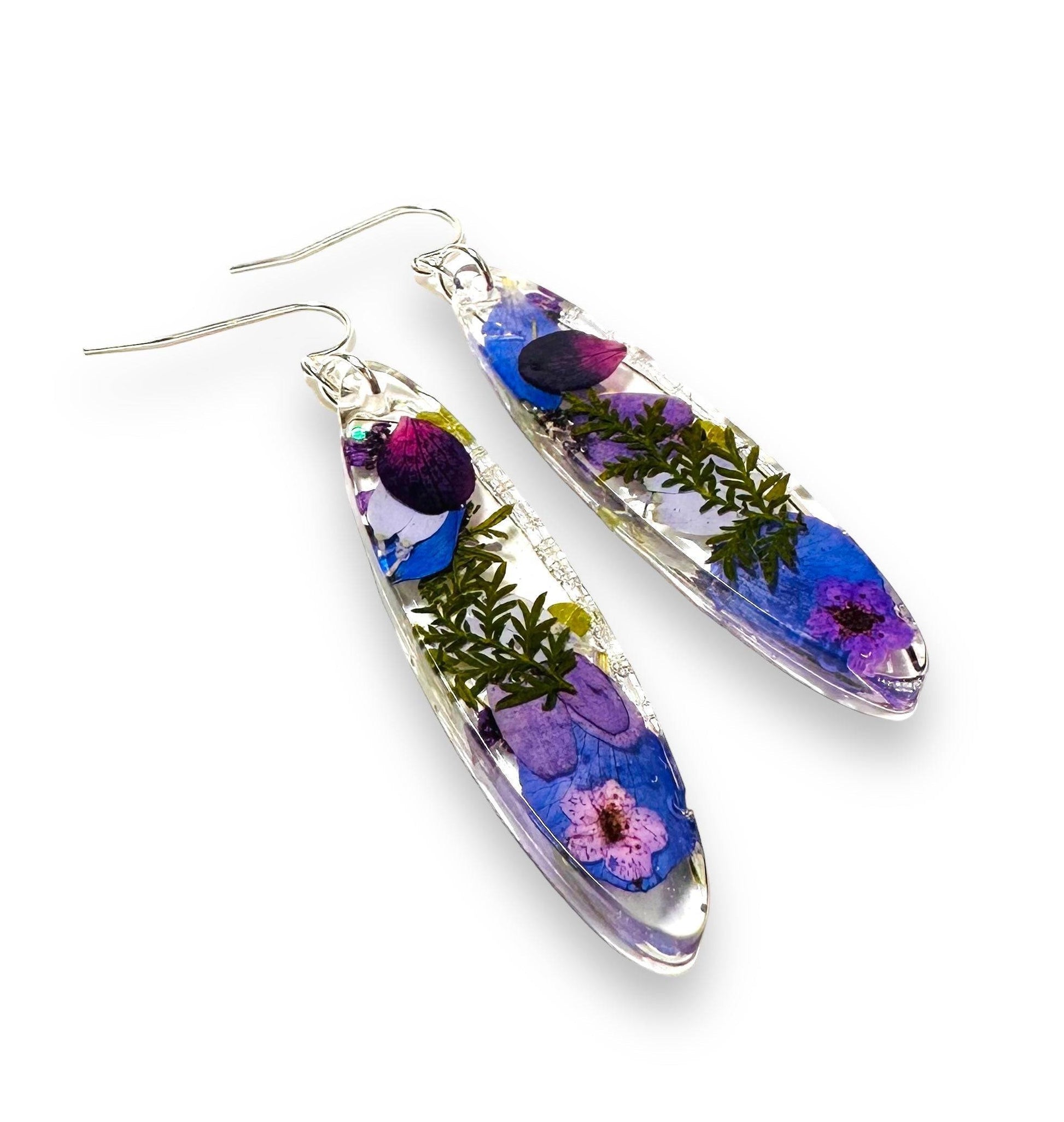 Long oval resin earrings with purple and blue real flowers and silver hooks. Botanical pressed flower earrings for a natural touch.