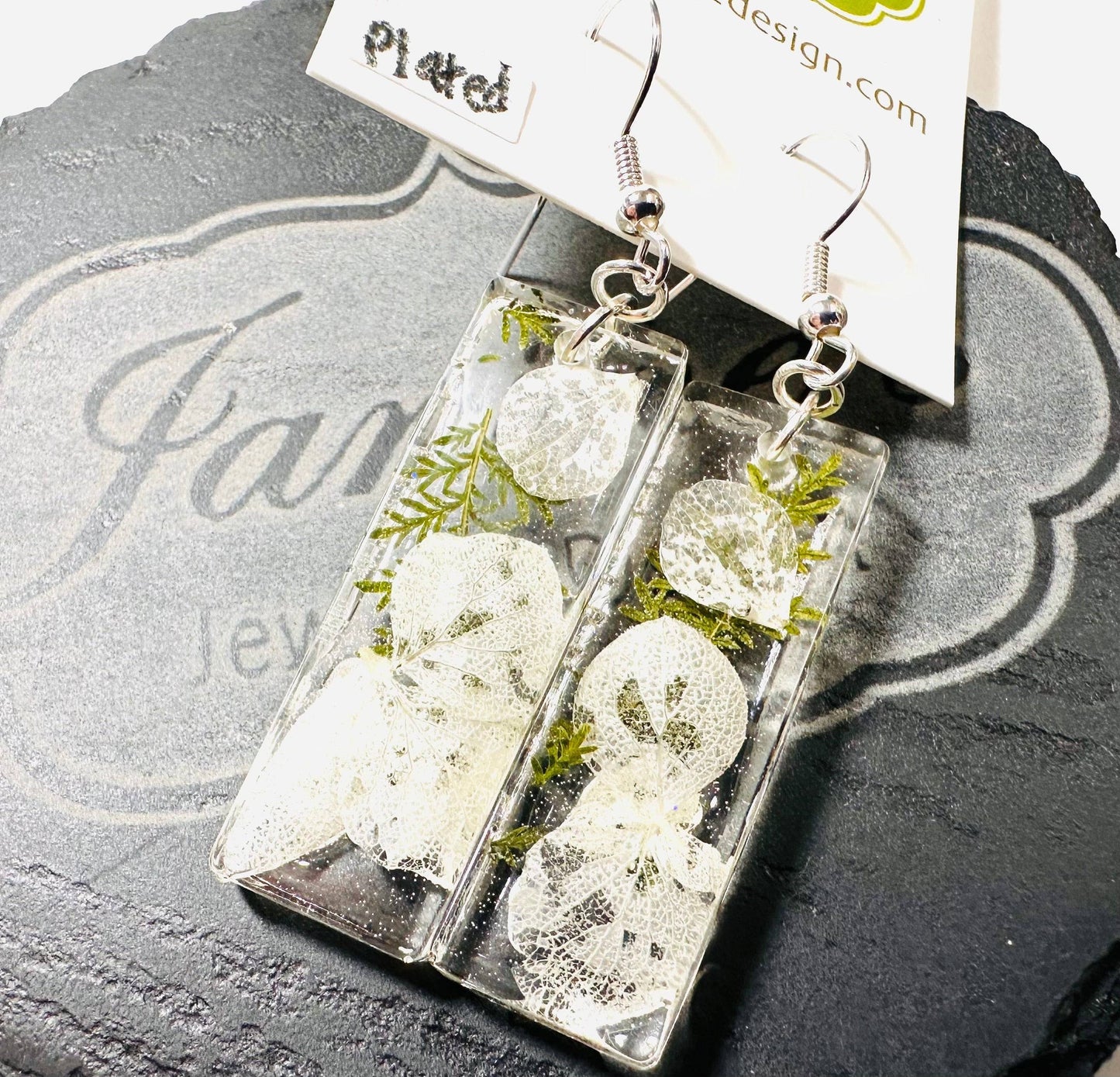 Rectangular resin earrings with white flowers and greenery and silver hooks. Elegant pressed flower earrings with a clean design.