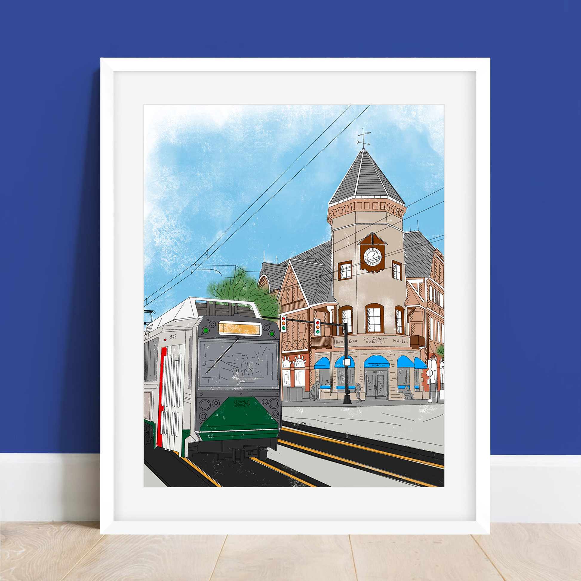 Coolidge Corner Art Print - 8x10 Matte Cardstock in a white frame against a blue wall, depicting a cityscape with trolley and iconic architecture.