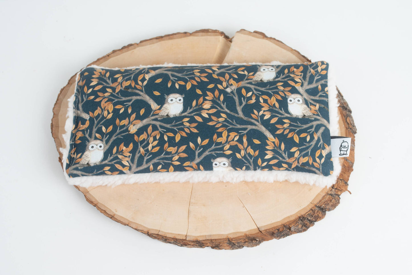 Weighted eye pillow with owl and autumn leaf pattern placed on a wooden tray, designed for stress relief and relaxation therapy.