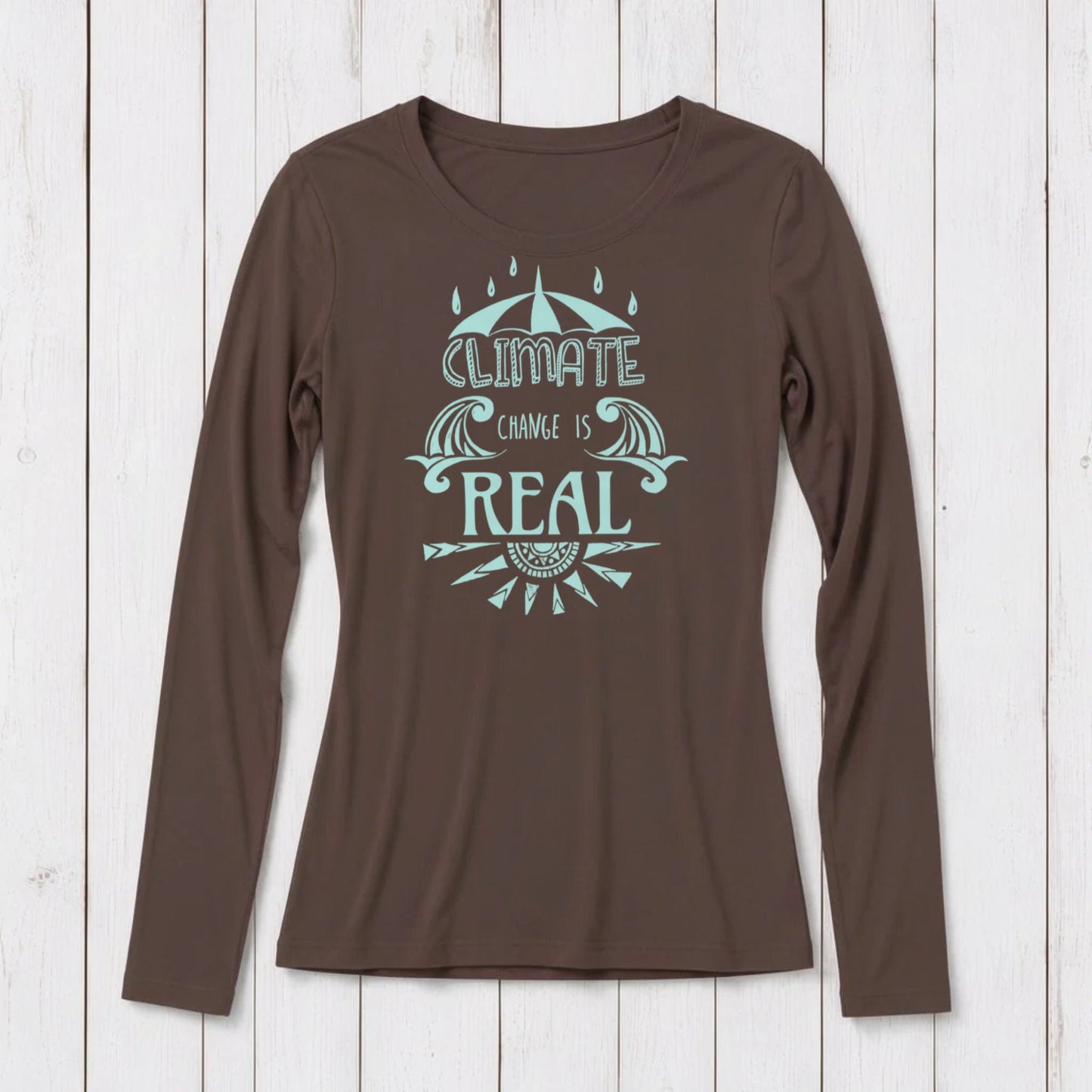 Brown long sleeve T-shirt with a light blue graphic design featuring an umbrella, waves, and the phrase 'Climate Change is Real' on a white wooden background