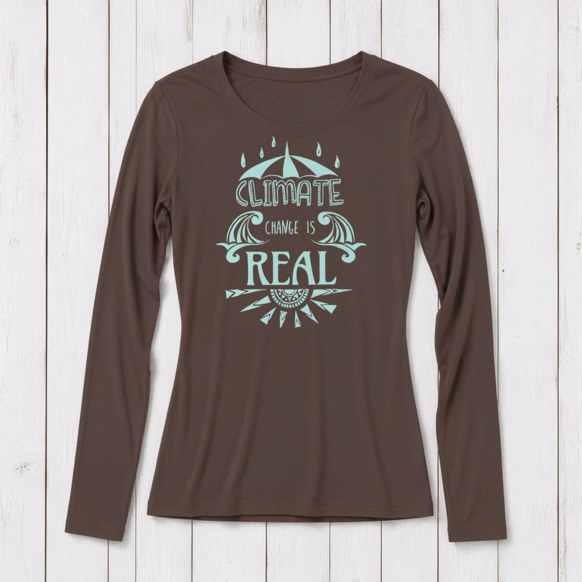 Brown long sleeve T-shirt with a light blue graphic design featuring an umbrella, waves, and the phrase 'Climate Change is Real' on a white wooden background