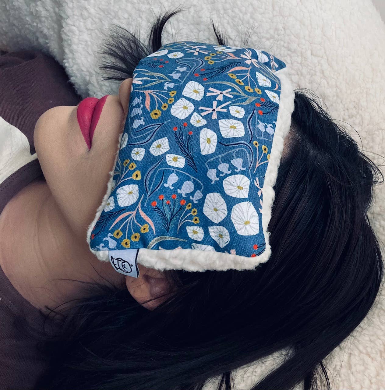 Woman using Deep Rest Eye Pillow with blue floral print while lying down, demonstrating its comfort and stress-reducing benefits.