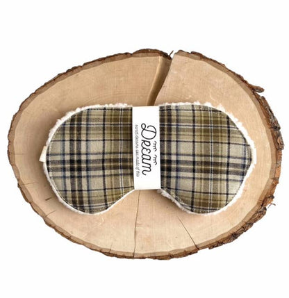 Plaid Cotton Sleep Mask for Relaxation featuring a green and beige tartan pattern, wrapped with branded label on a wood slice.