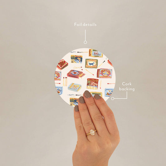 Hand holding Seedlings Coaster by Matchbooks showing foil details and cork backing, ideal for stylish barware protection.