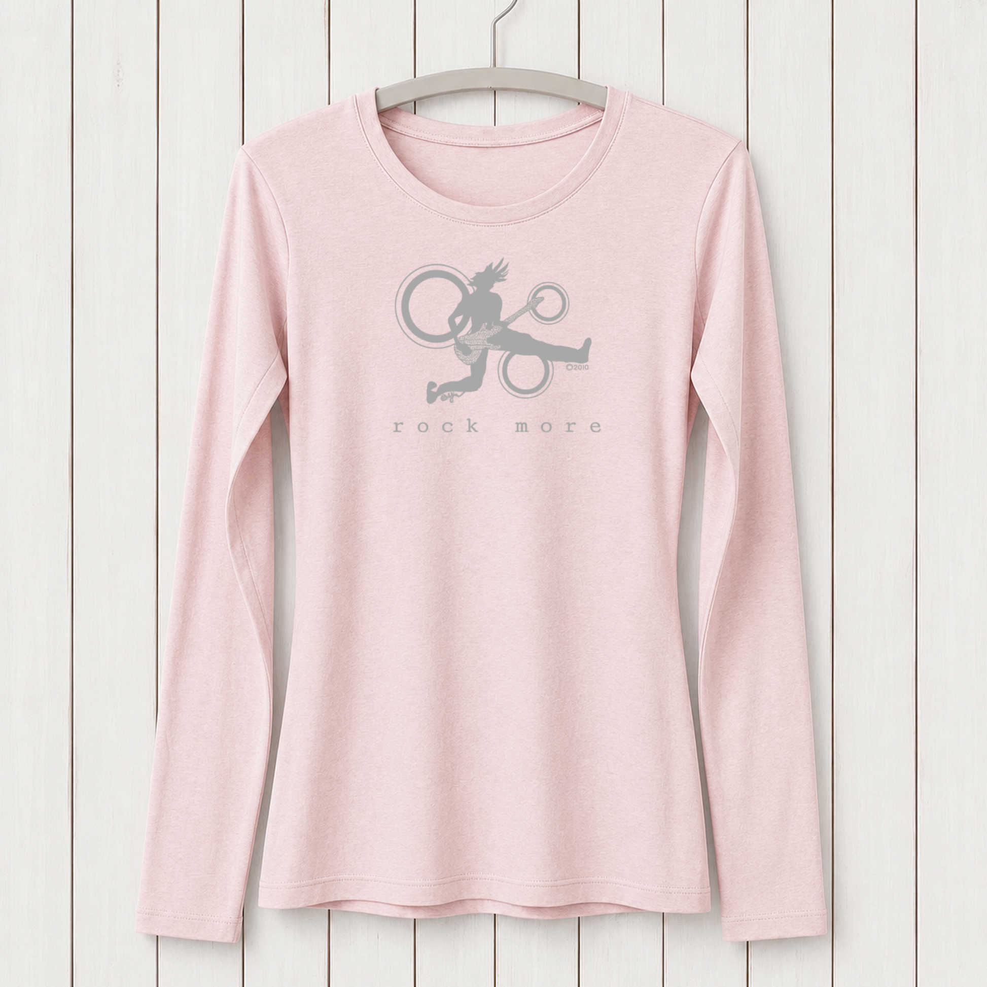 Light pink women's long sleeve T-shirt with a graphic of a rock musician playing guitar, hanging on a white wooden wall, eco-friendly fashion