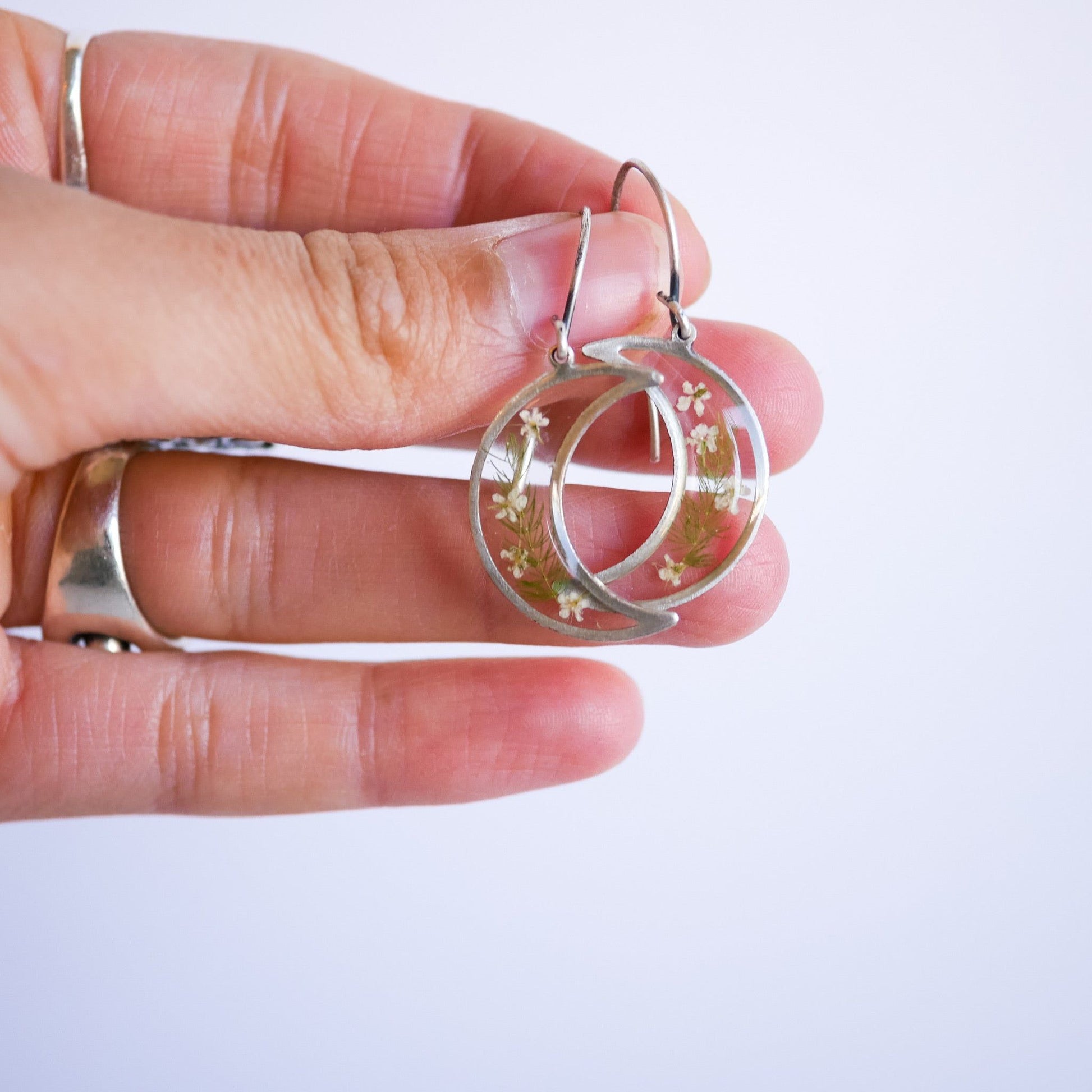 Silver Garden Flower Earrings with Queen Annes Lace held in hand. Crescent moon shape with delicate floral details, nickel free and unique.