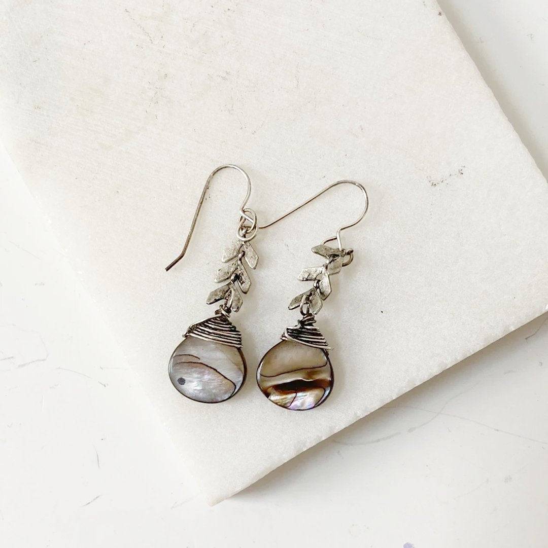 Abalone Chevron Earrings with sterling silver wire and darkened chevron brass, featuring teardrop abalone shells on a white marble background.