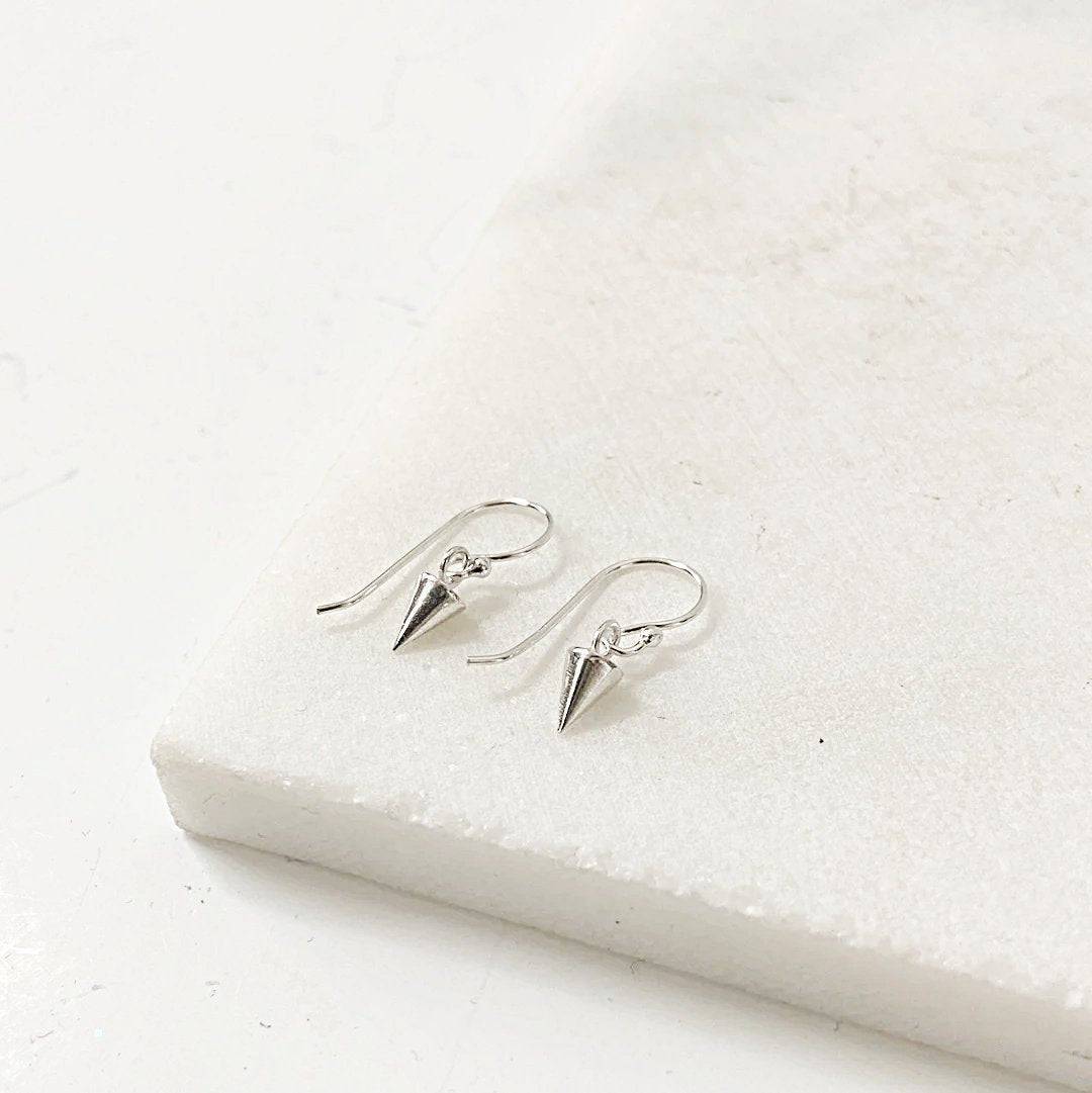 Tiny Spike Earrings-Uni-T - Sterling Silver earrings with minimalist cone-shaped spikes on hook backs, displayed on a white marble surface.