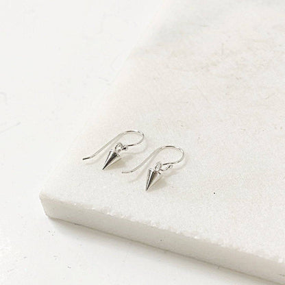 Tiny Spike Earrings-Uni-T - Sterling Silver earrings with minimalist cone-shaped spikes on hook backs, displayed on a white marble surface.