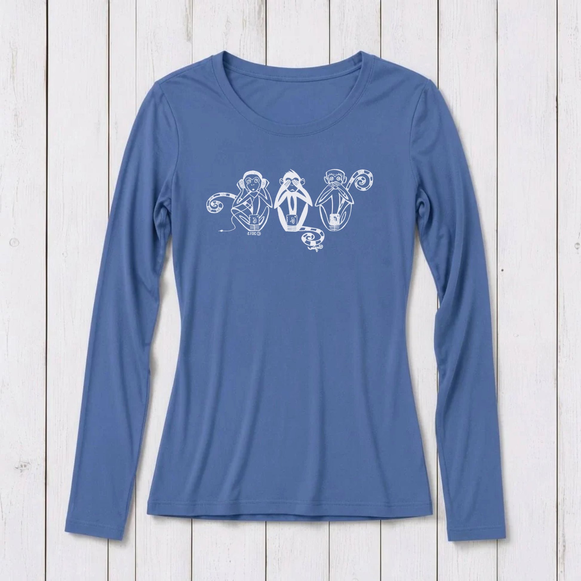 Blue long sleeve women's T-shirt with white graphic of three wise monkeys covering eyes, ears, and mouth, made from bamboo and organic cotton, on white wooden background