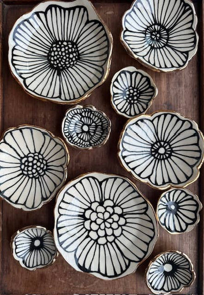 Set of 4" handmade flower-shaped ceramic dishes with black floral patterns and 22K gold accents, displayed on a wooden surface.