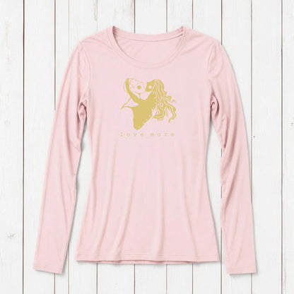 Light pink long sleeve T-shirt with a romantic gold graphic of a girl holding a heart-shaped balloon, featuring the words love more, on white wooden background