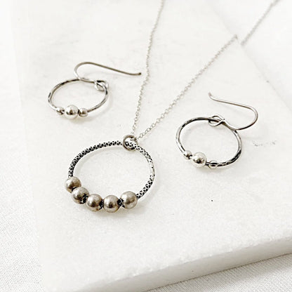 Circle Fidget Earrings & Necklace - Circle Fidget Jewelry Set with hammered metal texture and silver beads, laid flat on a marble surface.