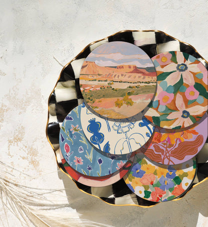 Assorted decorative coasters in a bowl, featuring corked-backed blue flower design among colorful artistic styles.
