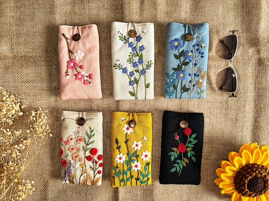 Set of six embroidered linen glasses cases with floral designs and button closures, offering stylish padded protection for eyewear.