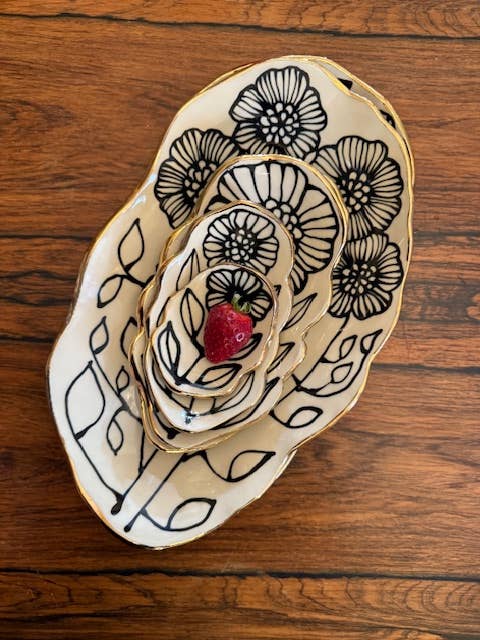 Stacked set of 5" handmade floral shaped 22K ceramic catchall jewelry dishes with black floral patterns and gold rims, topped with a strawberry.