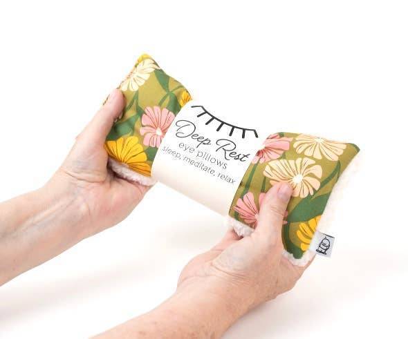 Hands holding Deep Rest Eye Pillow with green floral print, showcasing its soft texture and ergonomic design for sleep support.