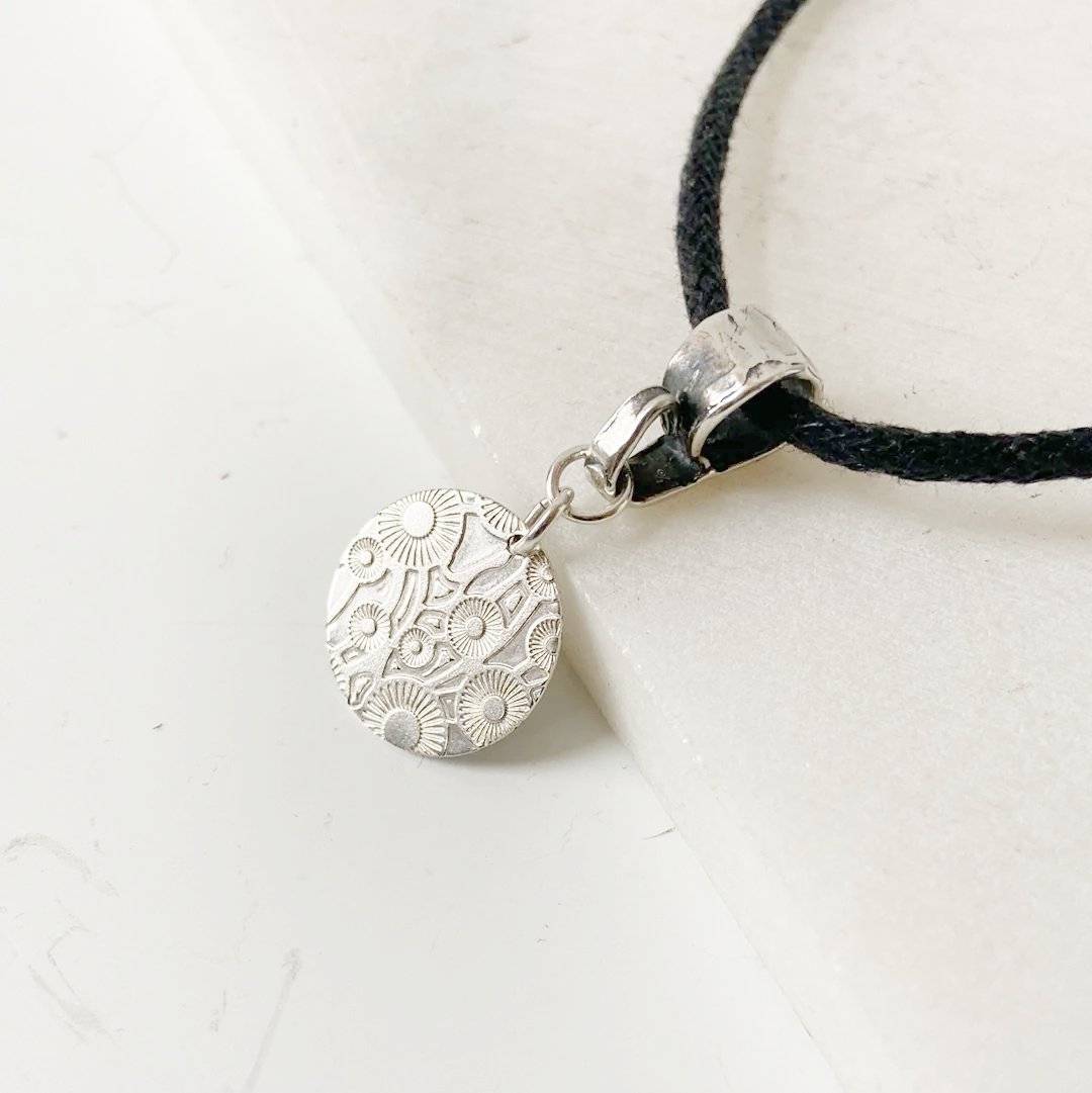 Close-up of Silver Dandelion Medallion Necklace showing intricate sterling silver dandelion pattern and sturdy clasp on 18-inch black cotton cord.