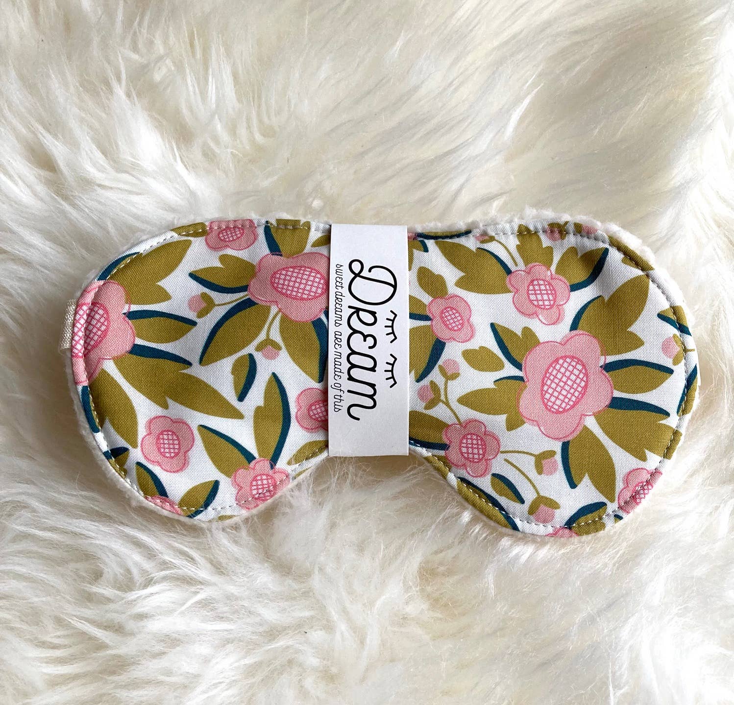 Sweet Dreams Cotton Sleep Mask featuring a pink and green floral design, laid on soft white faux fur for a cozy sleep accessory.