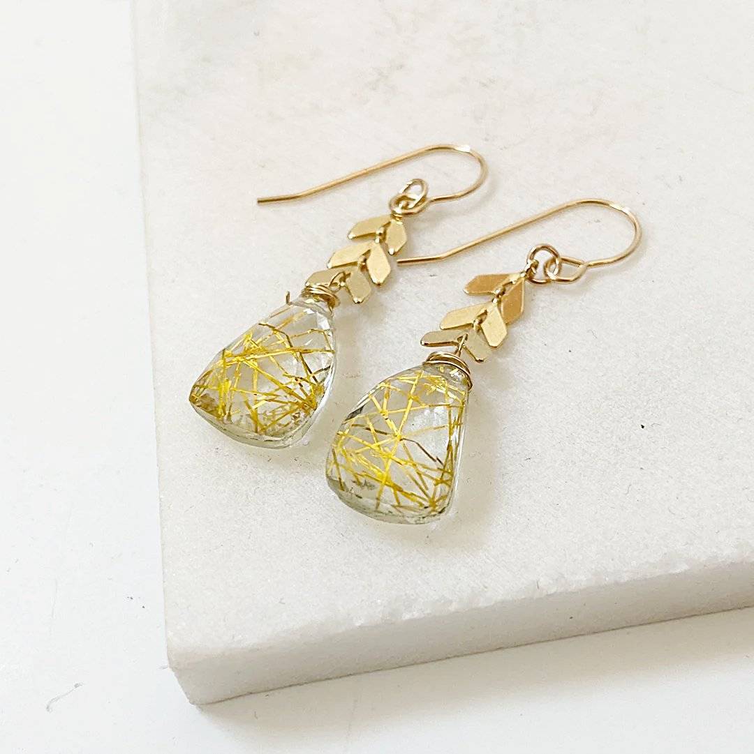 Close-up of Rutilated Quartz Chevron Earrings on marble background, showcasing golden rutile inclusions and chevron brass chain accents.
